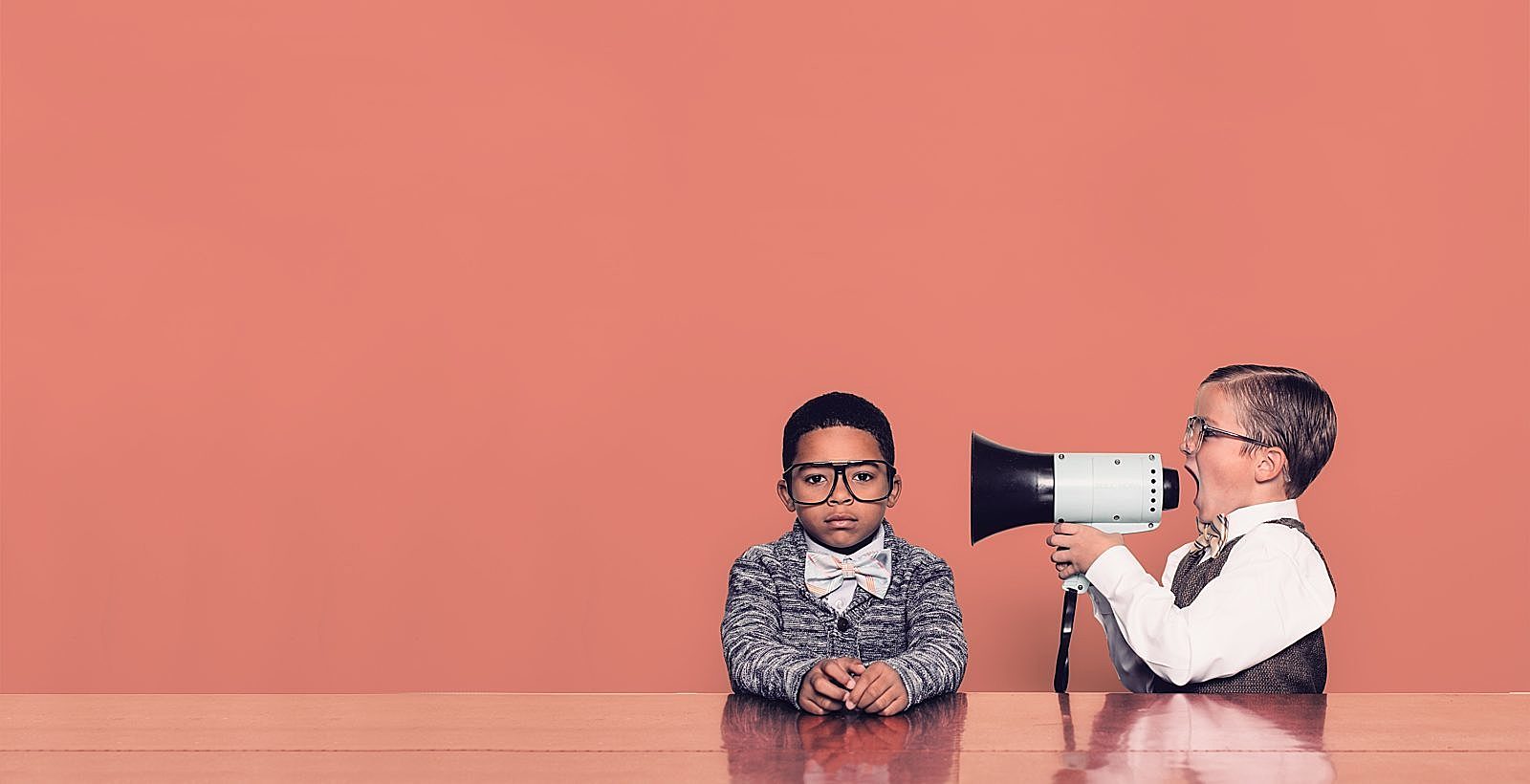 Child Yelling into a megaphone into another child's ear with red background